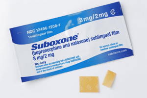 A single packet of an 8mg Suboxone film strip as well as a single film cut in half lay on a white background, intending to give the reader a visual of the medication that is at the center of the Suboxone lawsuit